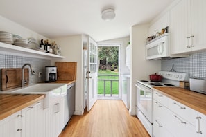 A kitchen with white cabinets, a wooden countertop, a built-in microwave, and a view to the outside.
