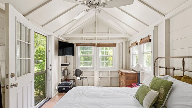 A bedroom with a bed, a desk, a chair, a ceiling fan, and a window with a view of greenery. - Charming property with 2 small cottages with 1-bedroom each in lovely Water Mill (Water Mill)
