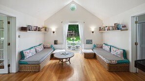A room with a high ceiling, a central table, two wicker sofas with patterned cushions, and bookshelves with books. - Charming property with 2 small cottages with 1-bedroom each in lovely Water Mill (Water Mill)