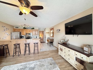 A modern kitchen with a bar area, wooden cabinets, a ceiling fan, and a flat-screen TV. - LOTO fun at 21 Lakeview Condo (Osage Beach)
