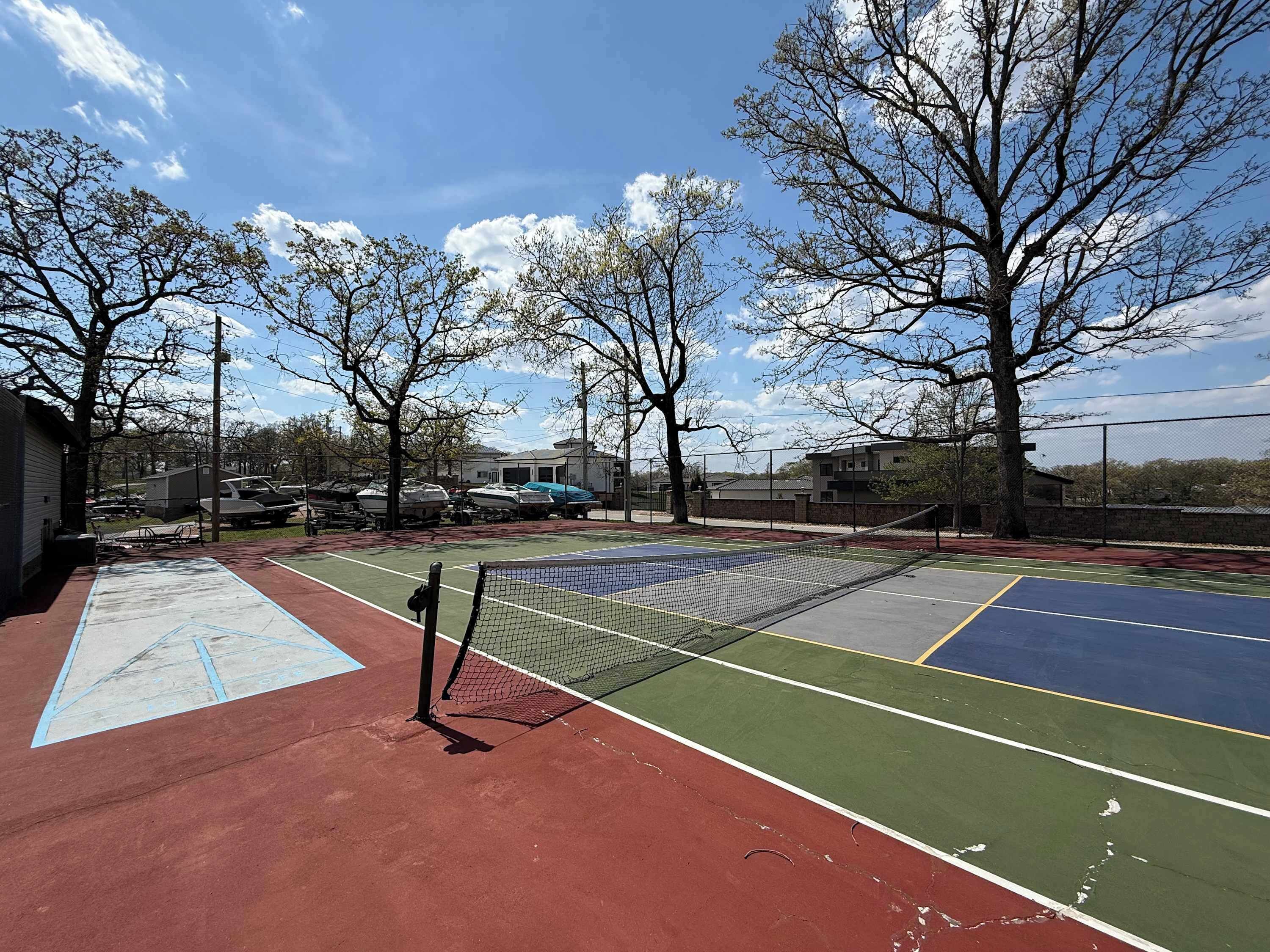 An outdoor tennis court with a net, surrounded by trees and buildings.