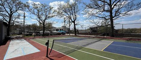 An outdoor tennis court with a net, surrounded by trees and buildings.