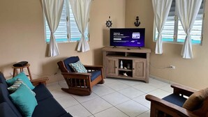 Una sala de estar con televisor, dos mecedoras, un sofá y un aparador.