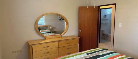 A bedroom with a bed, a dresser, a mirror, and an air conditioner.