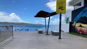 Una terraza de madera con vista al mar, un mural y un letrero que indica Plaza Ventana al Mar.