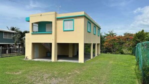 Un edificio de dos pisos con techo plano, un balcón en el nivel superior y un patio cercado.