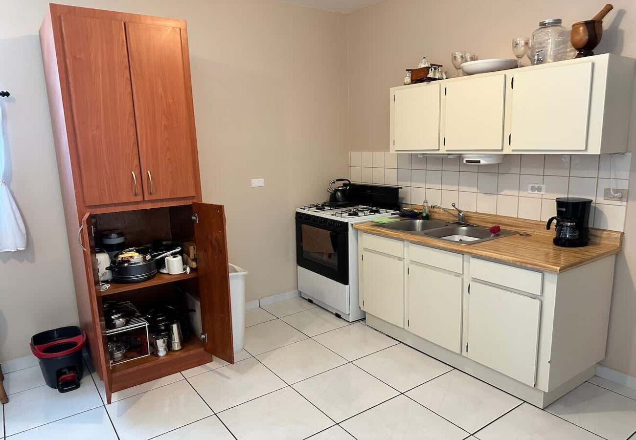 A kitchen with white cabinets, a stove, and a wooden cabinet with pots and pans.