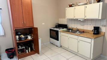 A kitchen with white cabinets, a stove, and a wooden cabinet with pots and pans.