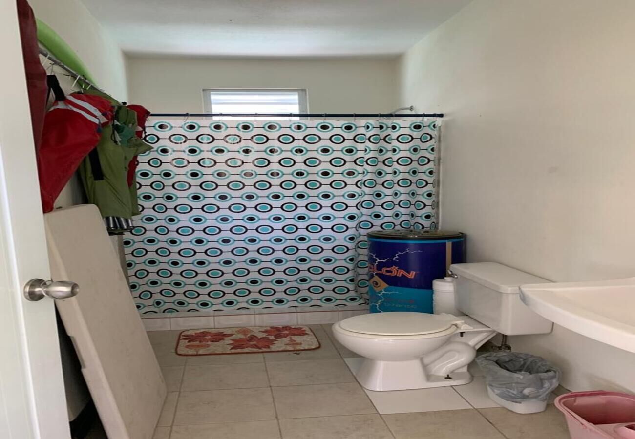 Ein kleines Badezimmer mit Toilette, Duschvorhang, Mülleimer und einer Tür.