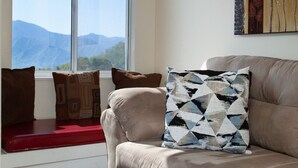 Ein Wohnzimmer mit einer Couch, einem Fenster mit Bergblick und einem Gemälde an der Wand.