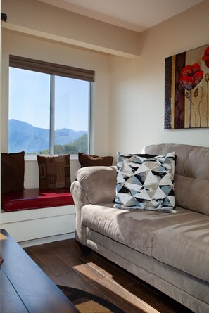 A living room with a sofa, a window with a view of mountains, and a painting on the wall. - Ski View LookOut: EPIC VIEWS! Community Amenities! (Gatlinburg)