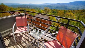 Ein Balkon mit Tisch, zwei Stühlen und Blick auf eine gebirgige Landschaft.