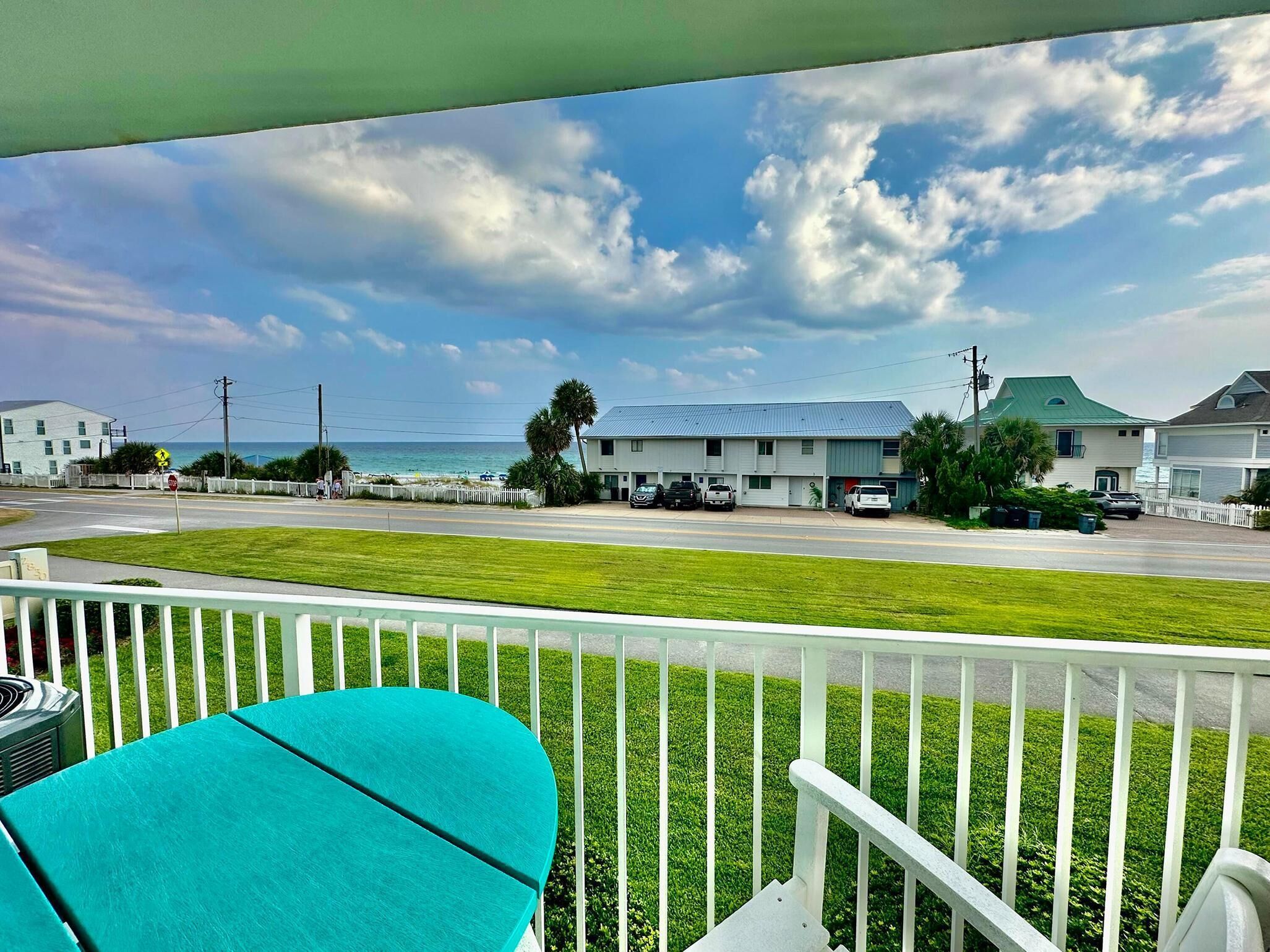 A view from a balcony overlooking a street with houses, a road, and the ocean.