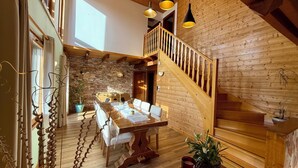 Een houten trap die leidt naar een eetgedeelte met een tafel en stoelen, een stenen muur en hangende lampen.