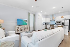 Ein modernes Wohnzimmer mit einer Couch, einem Fernseher und einem Essbereich, im Hintergrund eine Küche.