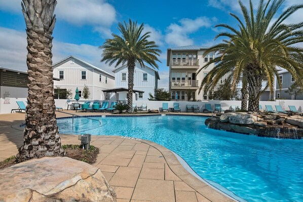 A swimming pool with lounge chairs and palm trees, surrounded by buildings with balconies. - Seabreezy (Santa Rosa Beach)