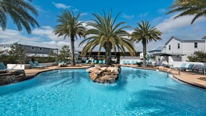 Piscina com espreguiçadeiras, palmeiras e um edifício ao fundo.