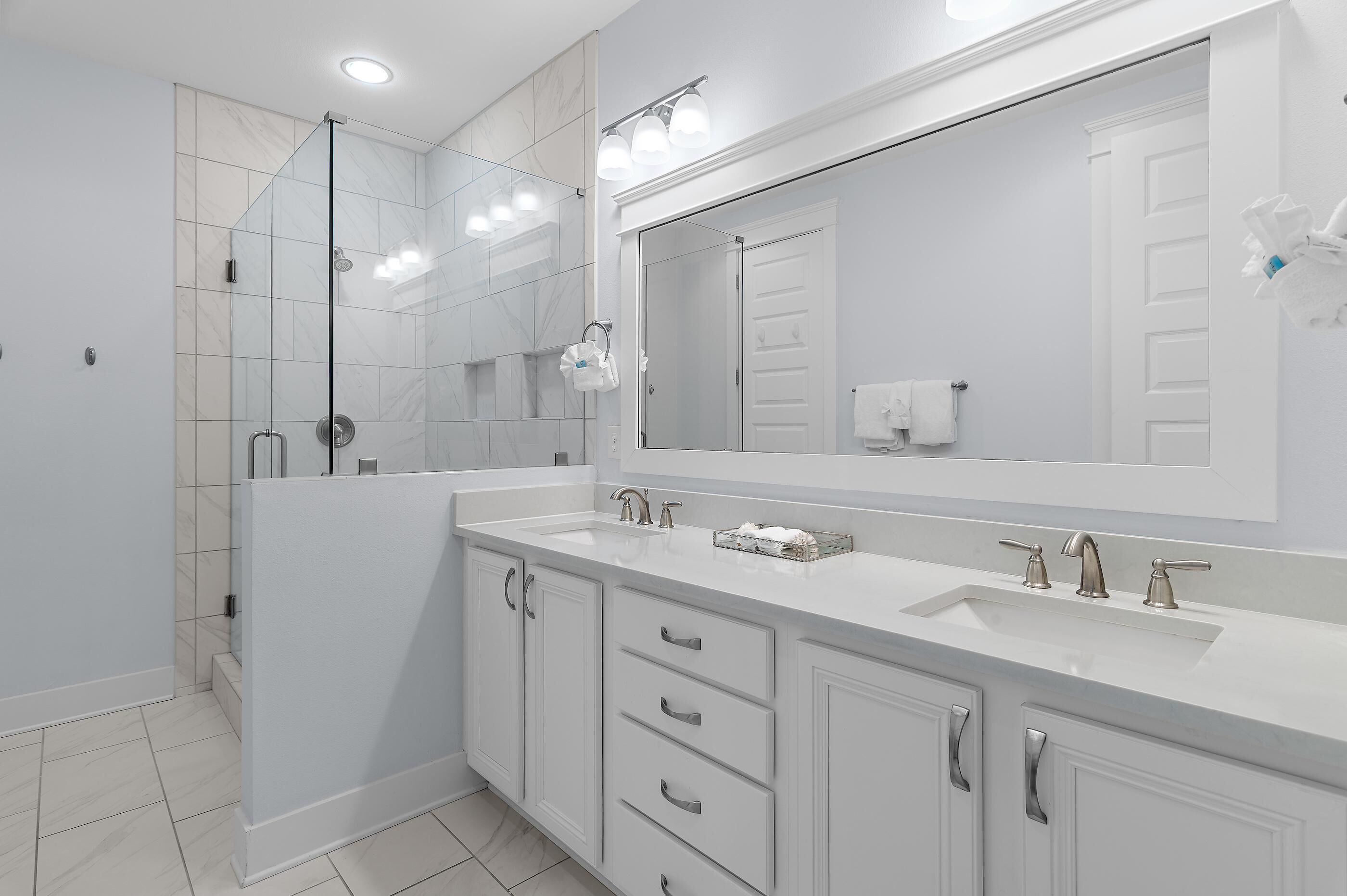 Un baño moderno con un espejo grande, dos lavamanos, una ducha y una cabina de ducha.