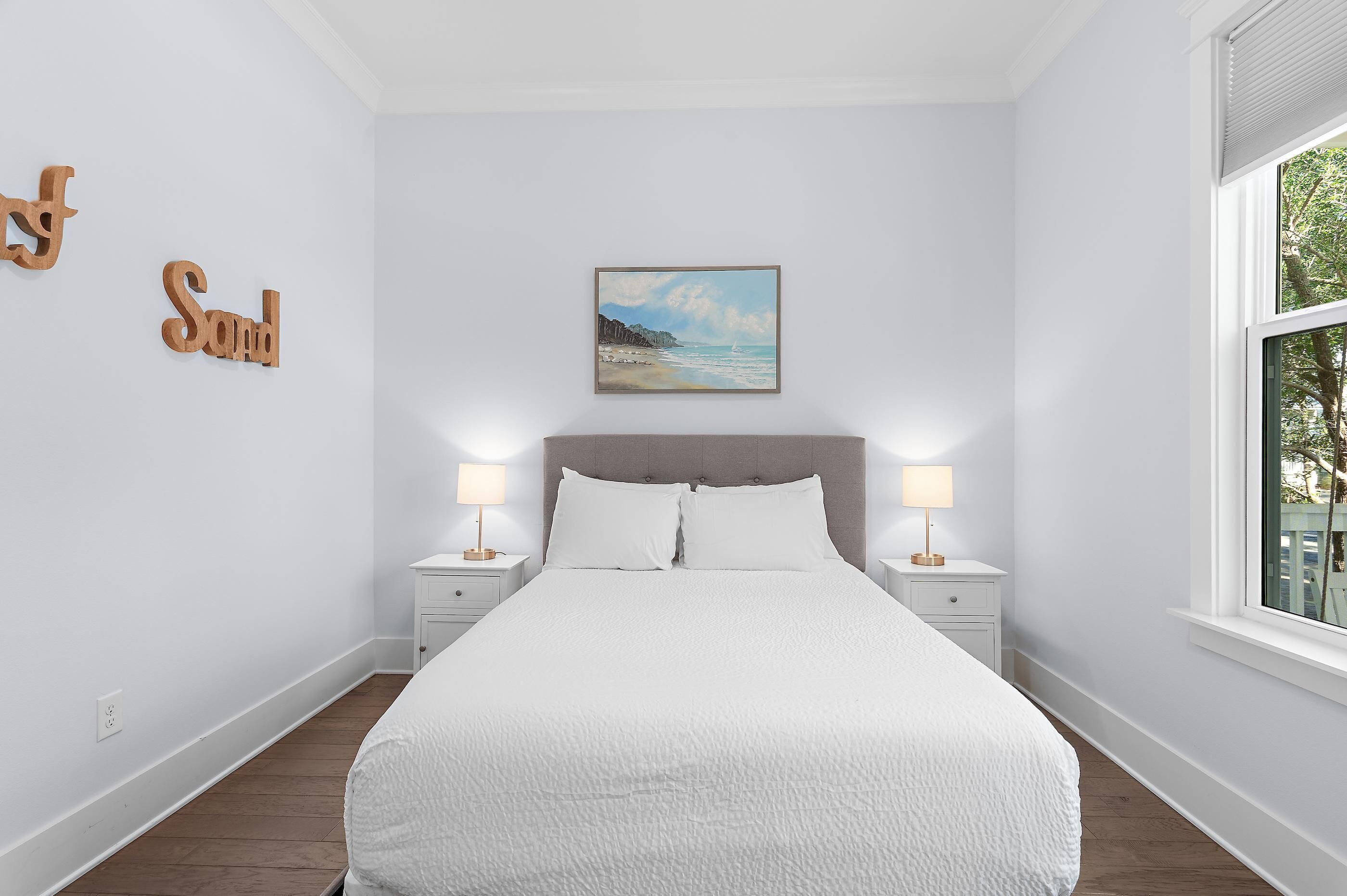 Un dormitorio con una cama, dos mesitas de noche con lámparas, un cuadro en la pared y una ventana.