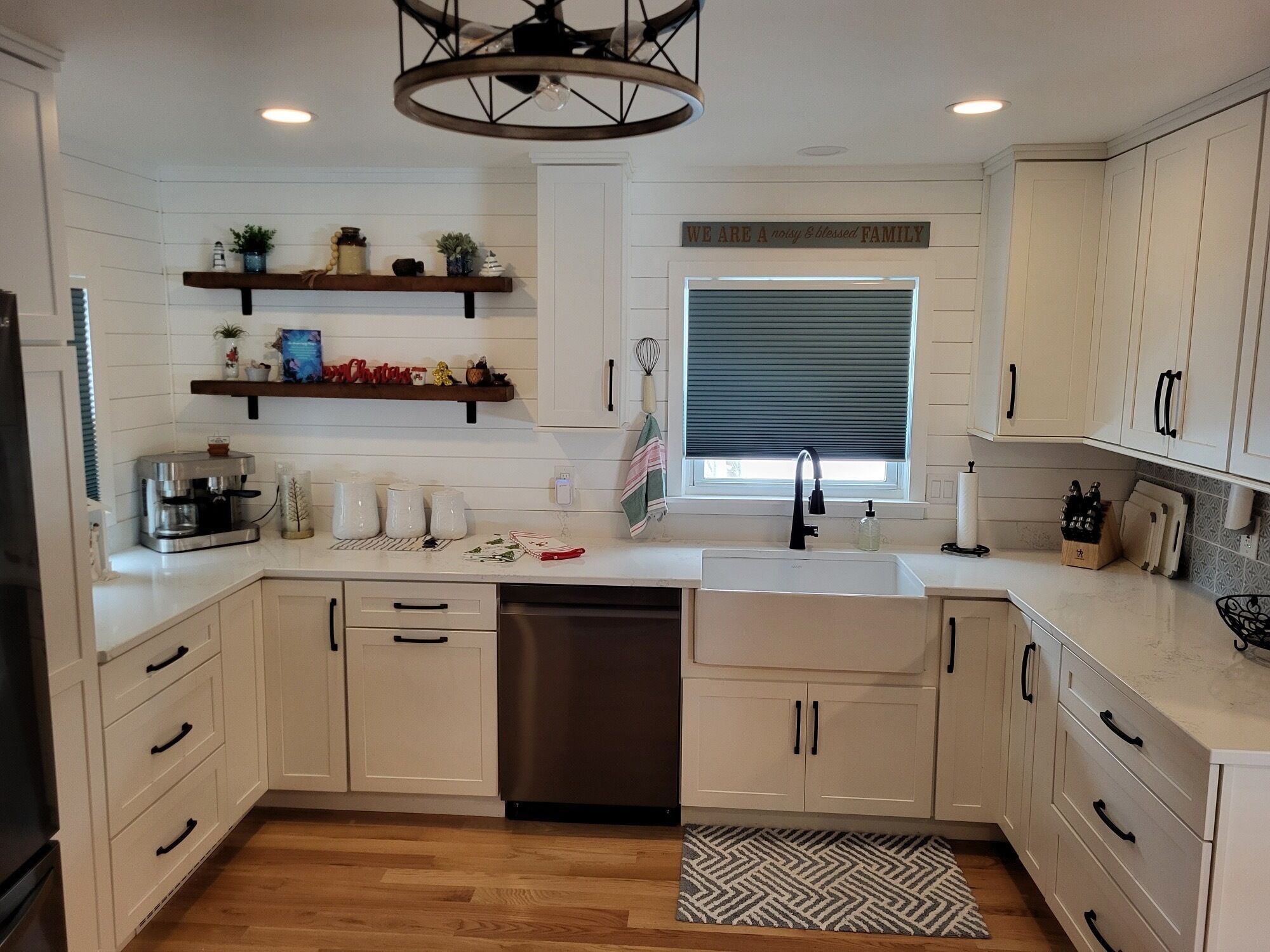 A kitchen with white cabinets, a dishwasher, a coffee maker, and a window with blinds.