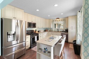 A kitchen with stainless steel appliances, a central island, and light-colored cabinetry. - Family Friendly Home Near Cedar Point & Downtown (Sandusky)