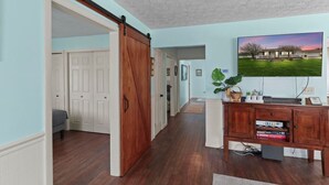 Un couloir avec une porte coulissante de style grange, un meuble en bois rempli de livres et un tableau encadré accroché au mur.