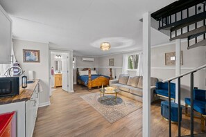 A modern living room with a wooden floor, a bed with a blue bedspread, a blue sofa, and a staircase. - Cozy Port Clinton Getaway w/ Hot Tub (Port Clinton)