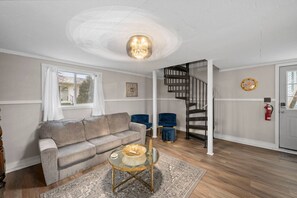 A living room with a sofa, a glass coffee table, a blue chair, a staircase, and a fire extinguisher. - Cozy Port Clinton Getaway w/ Hot Tub (Port Clinton)