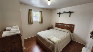 Un dormitorio con una cama de madera, una mesita de noche, una ventana con cortinas y una estantería sobre la cama.