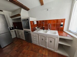 A kitchen with a refrigerator, oven, dishwasher, and a sink with a window above it. - Clair de Provence (Entrevennes)