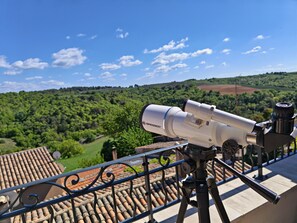 A telescope on a balcony with a view of a green landscape and a tiled roof. - Clair de Provence (Entrevennes)