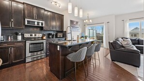 A modern kitchen with dark wood cabinets, stainless steel appliances, and a central island with bar stools. - Merlot | AC | Crib | Fenced Yard | Pets Ok (Calgary)