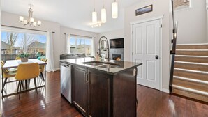 A modern kitchen with a central island, pendant lighting, and a view to the outside. - Merlot | AC | Crib | Fenced Yard | Pets Ok (Calgary)