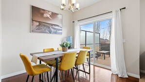 A dining area with a table, chairs, a chandelier, a painting, and a view through a glass door. - Merlot | AC | Crib | Fenced Yard | Pets Ok (Calgary)