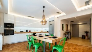 A modern kitchen with white cabinets, a wooden dining table, and green chairs. - MZ Kolonaki (Athens)