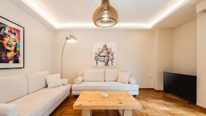 A modern living room with a sofa, a coffee table, a painting, a floor lamp, and a TV. - MZ Kolonaki (Athens)