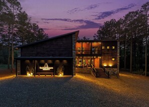A two-story lodge with a prominent front entrance, a staircase leading to the upper level, and a well-lit driveway. - Luxury Resort | Golf Sim, Pool, Gym, Sauna, 30 ppl (Broken Bow)