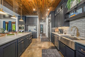 A modern kitchen with dark cabinetry, stainless steel appliances, and a wooden ceiling.