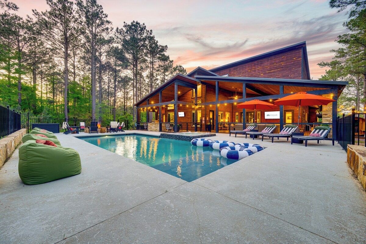 Un chalet moderne doté d’une piscine, d’un espace extérieur aménagé et offrant une vue sur de grands arbres.