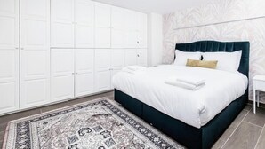 A bedroom with a bed, a white wardrobe, a patterned rug, and a wall with a leaf pattern. - MZ Kolonaki Hills (Athens)