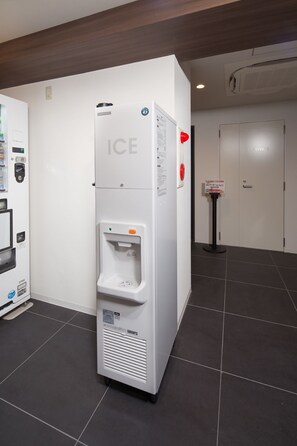 A white ice dispenser with a push button, a private elevator sign, and a vending machine to the left. - Hotel Meldia Kyoto Shijo Omiya (Kyoto)