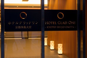 To hotelskilte, hvor det ene viser 'Hotel Grand Warsaw' og det andet 'Hotel Glad One - Kyoto Shijo Omiya', skrevet på engelsk og japansk.
