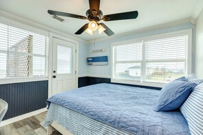 A bedroom with a bed, a ceiling fan, a window with blinds, and a door.