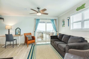 A living room with a ceiling fan, a sofa, a chair, a desk, and a view of the balcony.