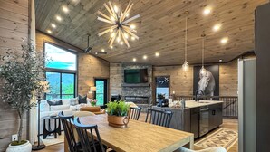 A modern kitchen with a wooden ceiling, a dining area with a large table and chairs, and a living room with a sofa and a fireplace. - Best Views • Indoor Pool • Hot Tub • Romance (Sevierville)
