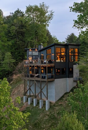A modern two-story house with a balcony, surrounded by trees.