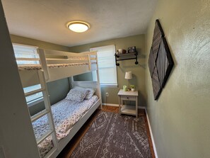 Habitación con literas, una mesita, una lámpara y una repisa con objetos decorativos.