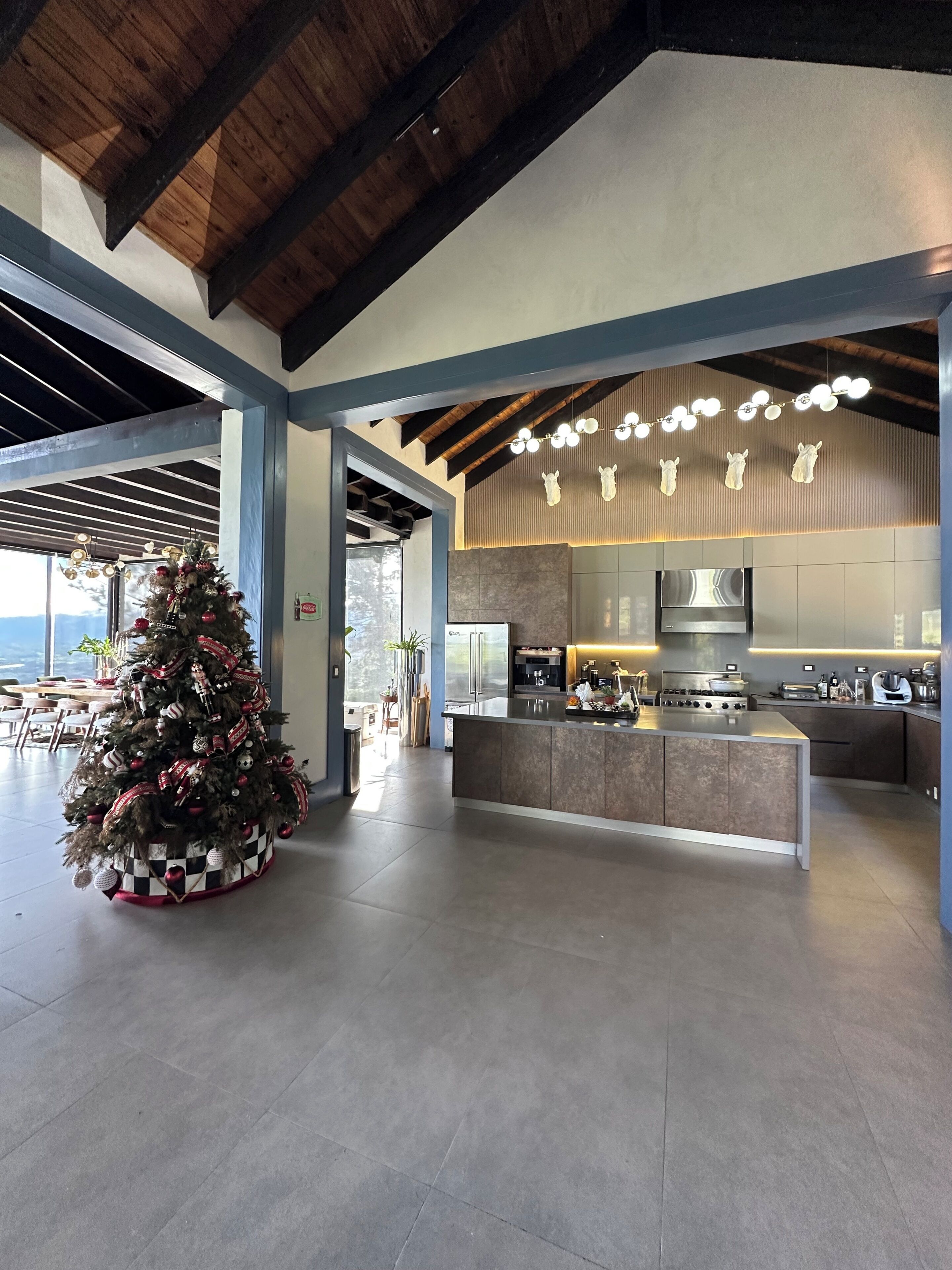 A modern kitchen with a large island, a Christmas tree, and a view of the outdoors.