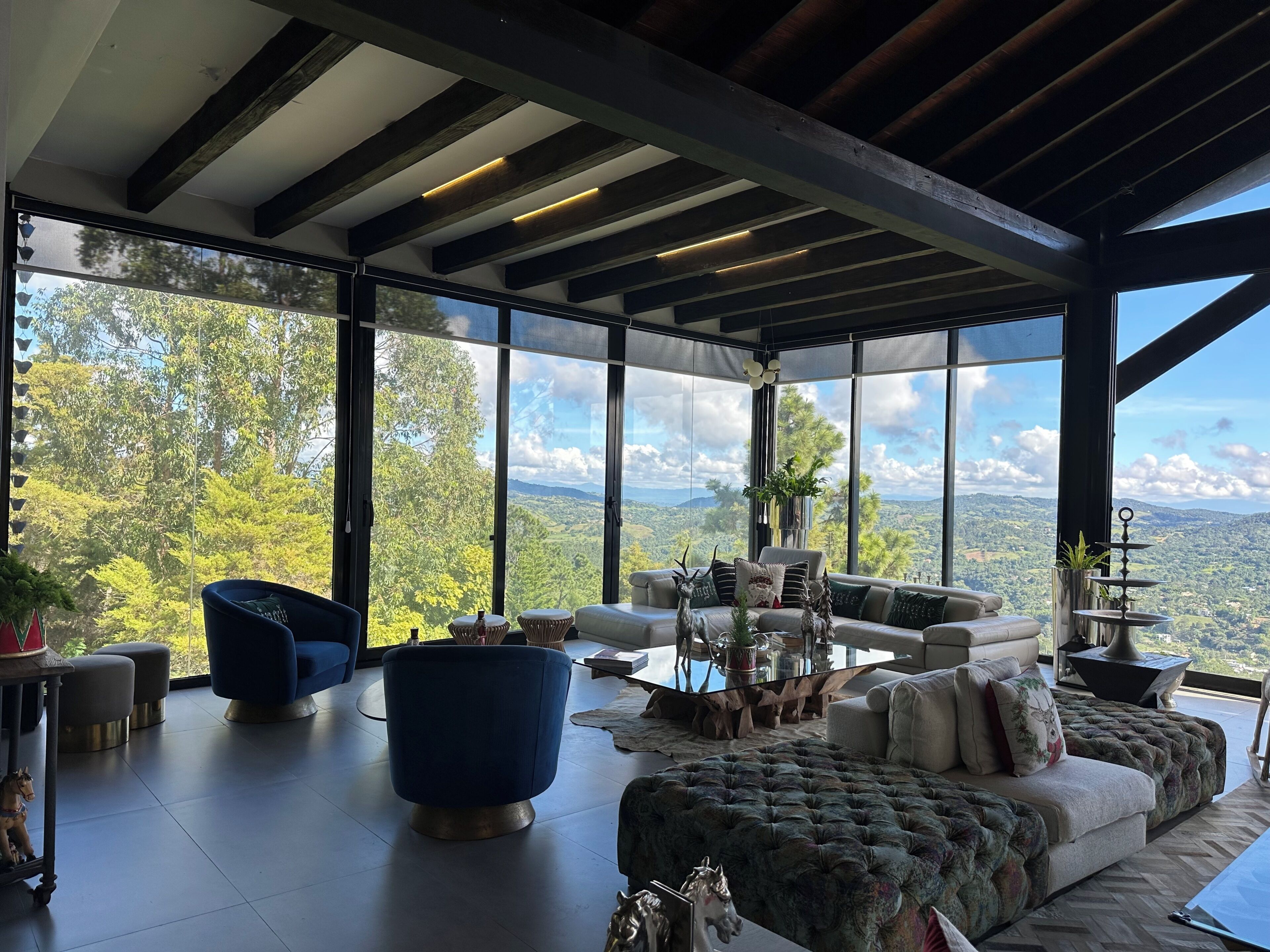A spacious living area with a large window offering a scenic view, a modern sofa, a blue armchair, and a glass coffee table.