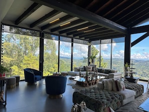 Ein großzügiger Wohnbereich mit einem großen Fenster und herrlicher Aussicht, ein modernes Sofa, ein blauer Sessel und ein Glastisch.